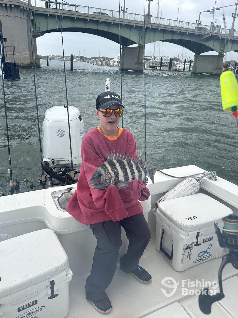 Young angler proudly holding a striped Sheepshead while fishing near a bridge, showcasing a successful catch on a charter trip.