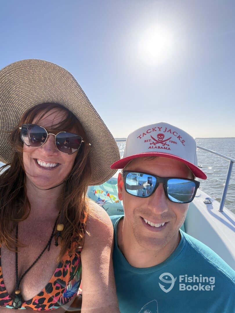 Two smiling individuals enjoying a sunny day on a boat, with the sun shining brightly in the background.