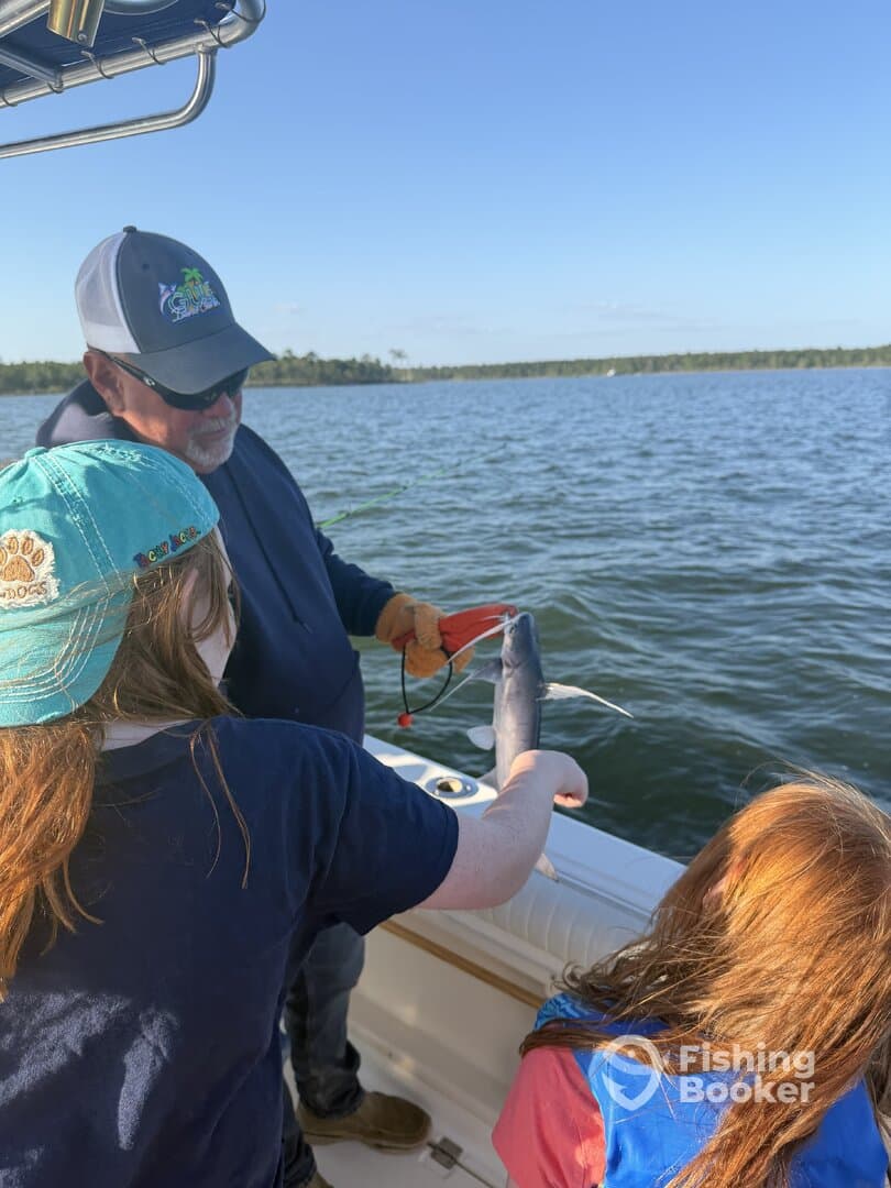 A family enjoys a fishing trip, with a child proudly holding a caught fish while on a boat in a scenic waterway.