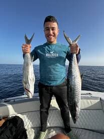 Angler proudly displaying two large fish, a King Mackerel and a Grouper, while fishing offshore.