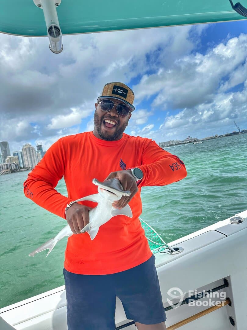 Angler proudly displaying a small shark while fishing on a boat in a vibrant coastal setting.