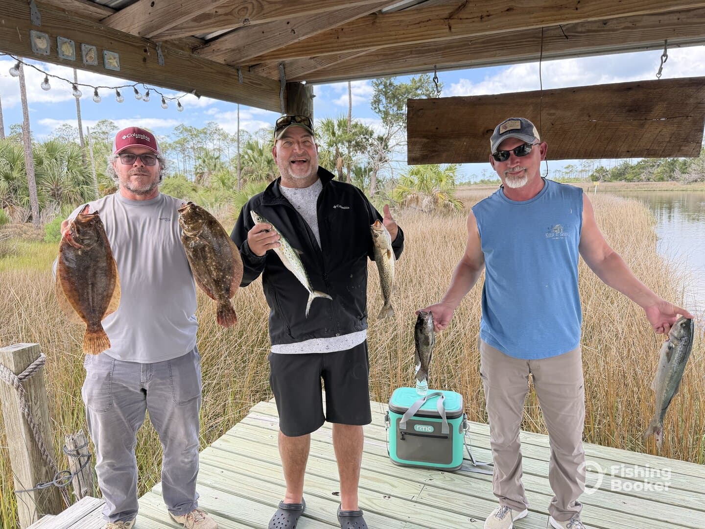 Three anglers proudly displaying their catch of Flounder and Speckled Trout on a dock in a coastal fishing environment.