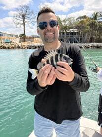 A proud angler displaying a striped fish while fishing from a dock, with a scenic waterfront in the background.