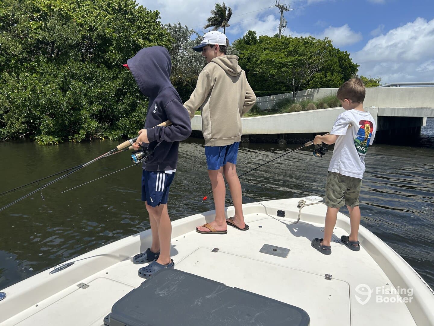 Three young anglers casting lines from the bow of a boat in a calm waterway, enjoying a day of fishing.