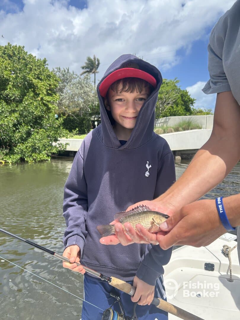 A young angler proudly holding a small fish while fishing in a scenic waterway, showcasing a fun day out on the water.