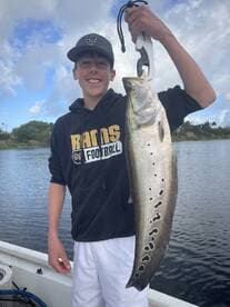 A young angler proudly displaying a large Speckled Trout while fishing on a calm waterway.