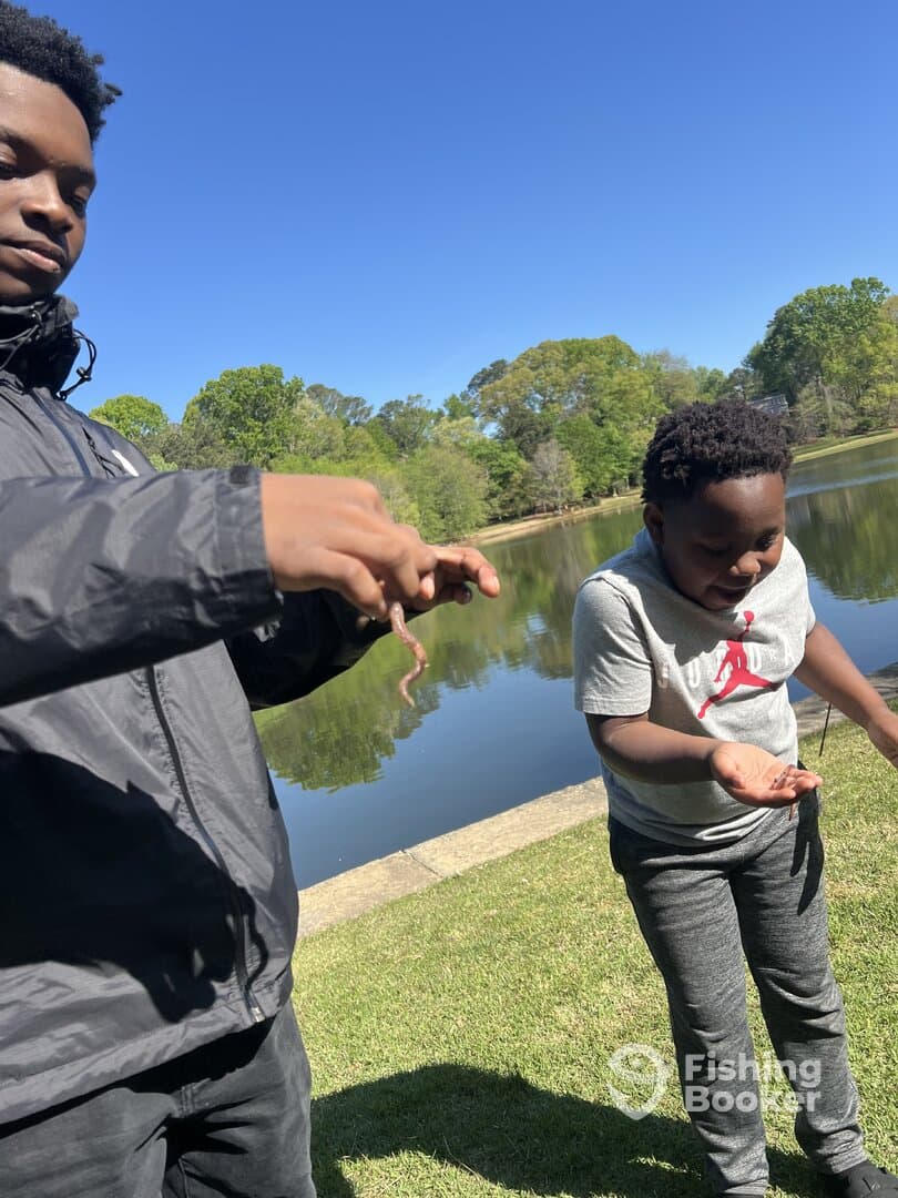 Two individuals enjoying a day by the water, with one holding a worm while the other looks on, showcasing a casual fishing experience.