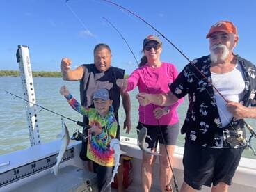 A family group proudly displaying their catch of fish while fishing on a boat in a sunny coastal environment.