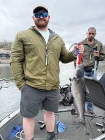 Angler proudly displaying a large Catfish while fishing on a boat, showcasing a successful day on the water.