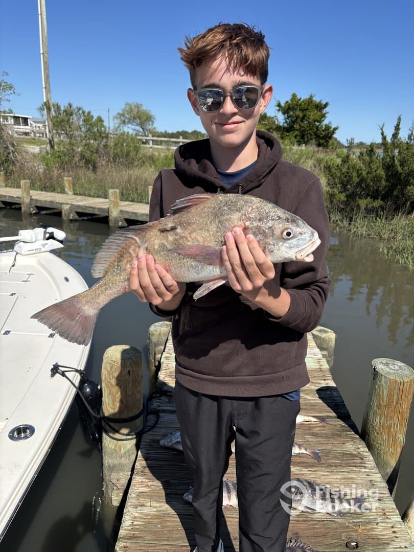 Young angler proudly holding a large fish on the dock, showcasing a successful day of fishing.