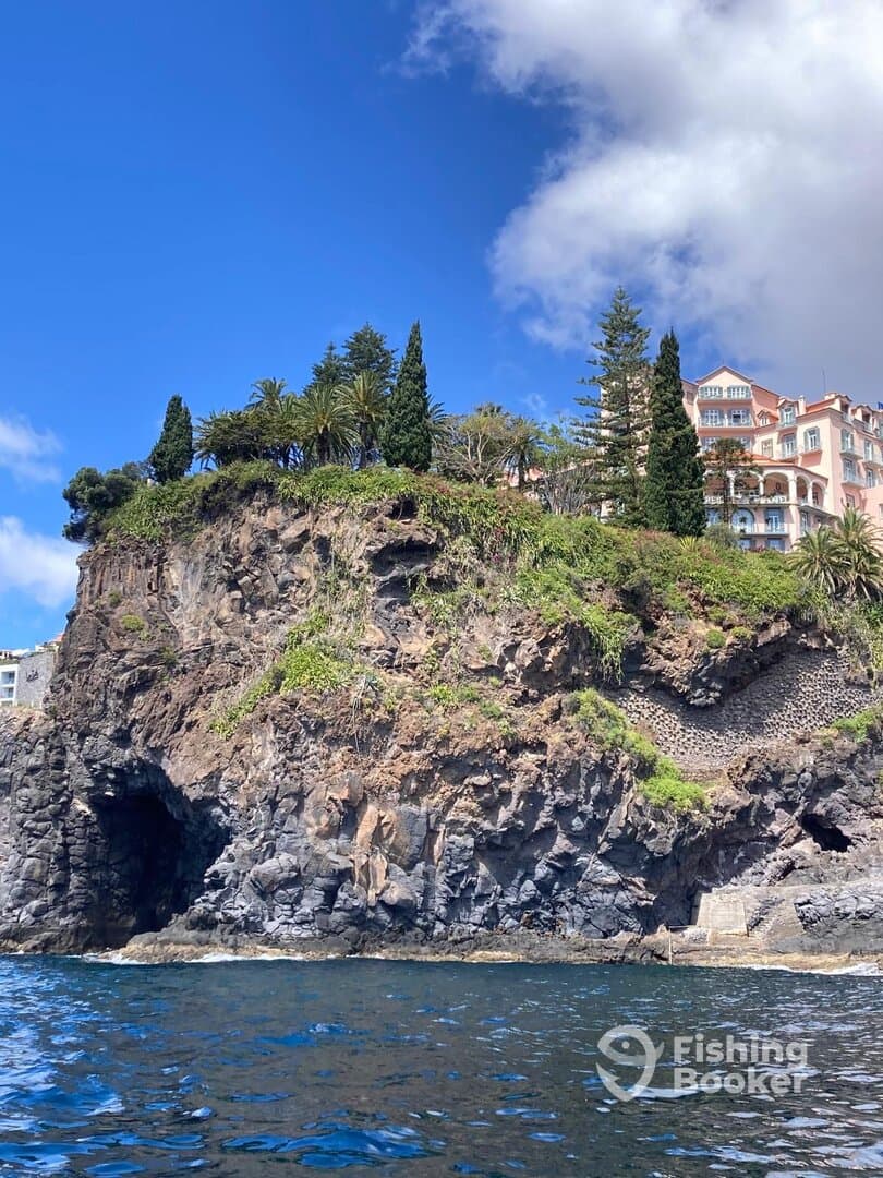 Scenic view of a rocky coastline with lush vegetation and a beautiful building, captured from the water.