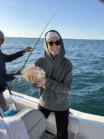 A happy angler proudly displaying a Snapper while fishing on a boat, enjoying a sunny day on the water.