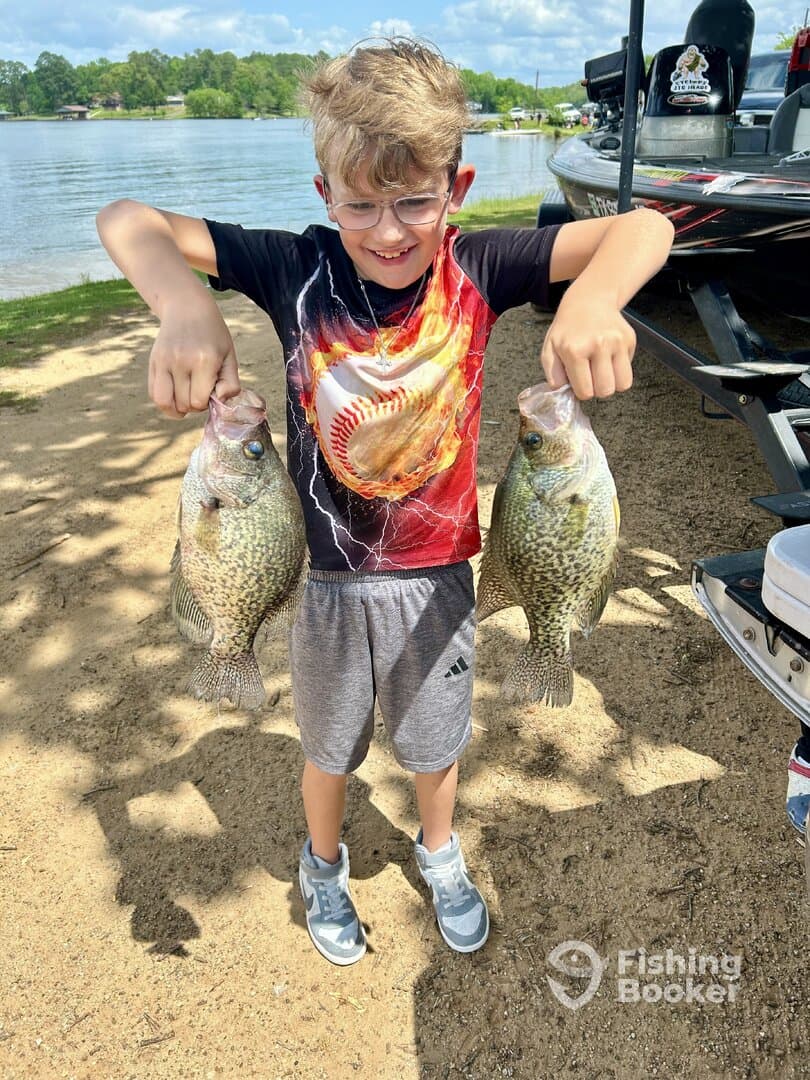 A young angler proudly displaying two Crappie caught during a fun day of fishing at the lake.