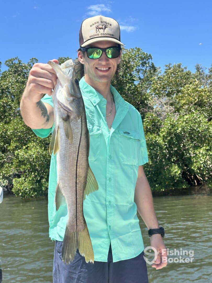 Angler proudly displaying a large Snook while fishing in a scenic coastal environment.