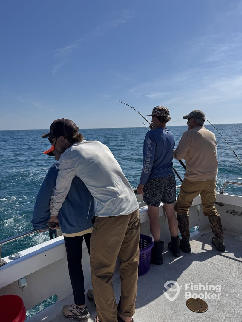 A group of anglers enjoying a fishing trip on a boat, actively engaged in reeling in their catch while surrounded by the open sea.