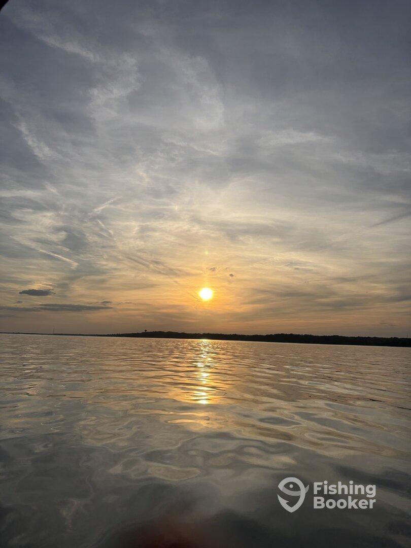 A serene sunset over calm waters, reflecting the vibrant colors of the sky, creating a picturesque fishing environment.