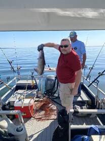 Angler proudly displaying a large catfish while fishing on a calm day, showcasing a successful outing with friends.