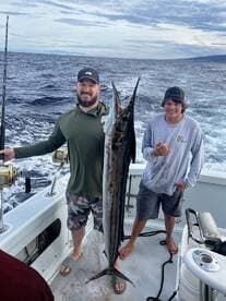 Two anglers proudly displaying a large Mahi-Mahi on a fishing charter in open waters.