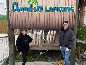 Two anglers proudly posing in front of a catch board displaying several Redfish at Chandlers Landing.