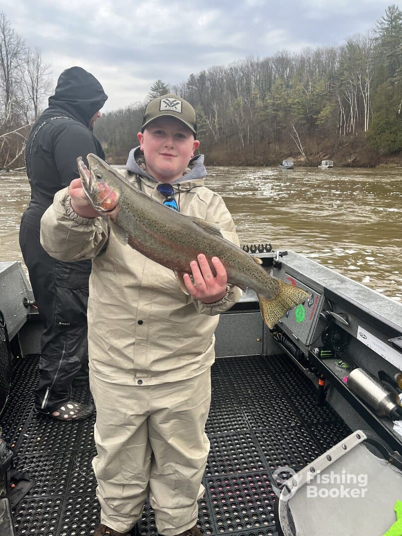 A young angler proudly displaying a Rainbow Trout while fishing on a river, showcasing the excitement of a successful catch.