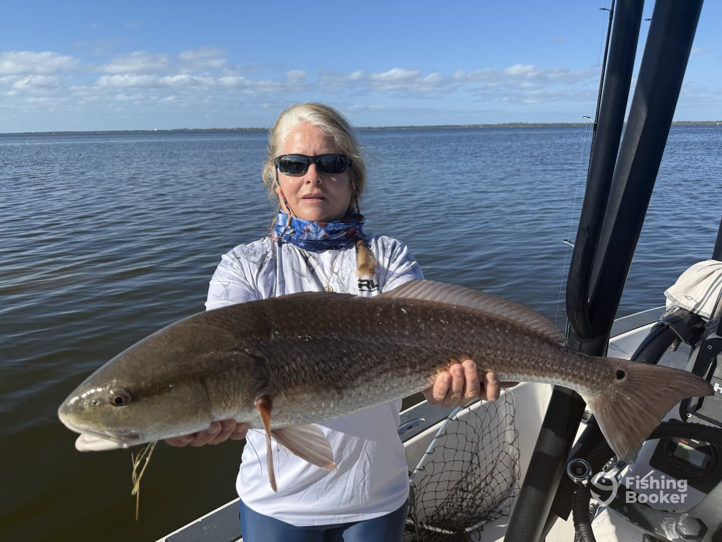 Angler proudly displaying a large Redfish while fishing on a boat in calm waters.