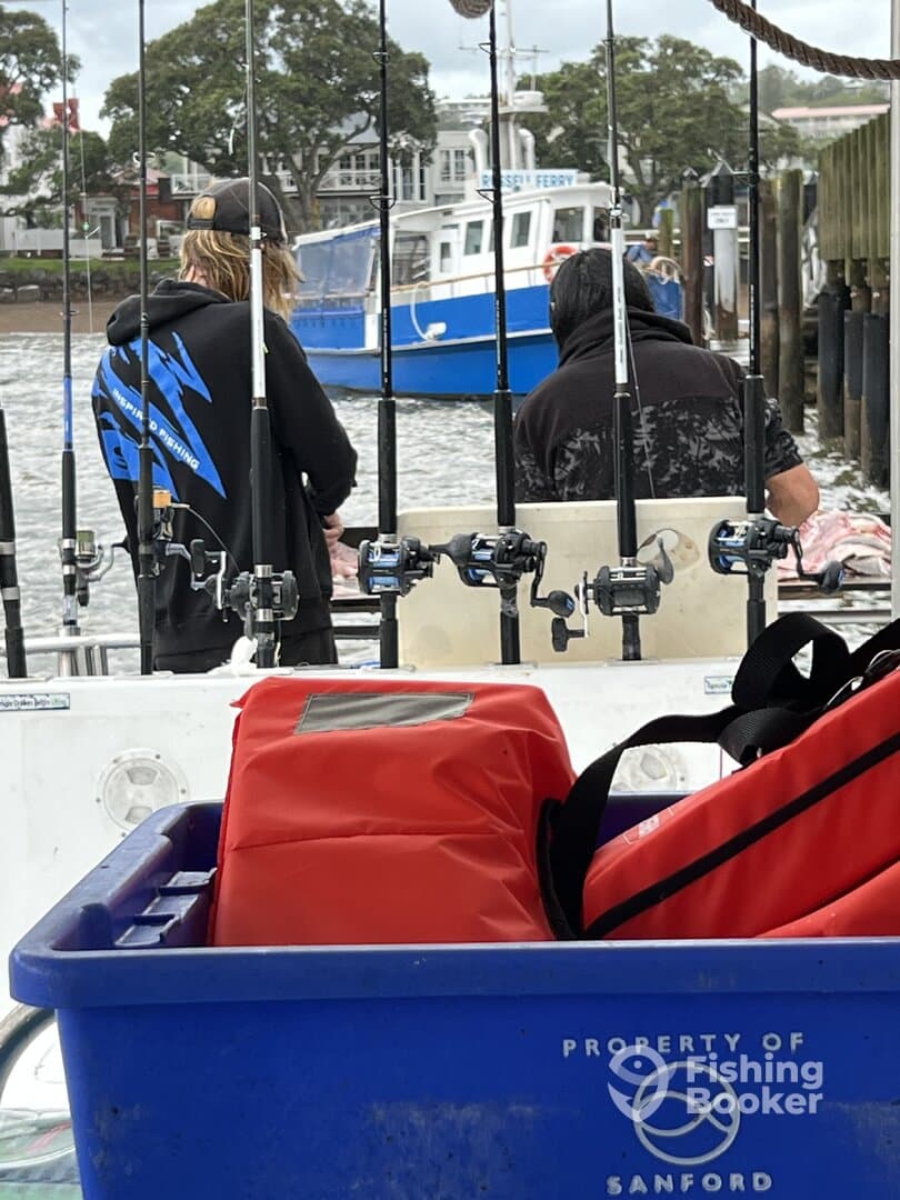 Two anglers preparing for a fishing trip on a boat, with fishing rods visible and a scenic waterfront in the background.