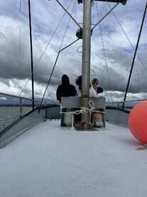 Two individuals seated on the boat, enjoying the view of the water and cloudy skies.