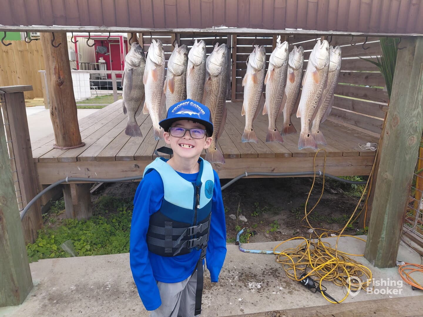 A young angler proudly poses in front of a catch board displaying several Redfish after a successful fishing trip.