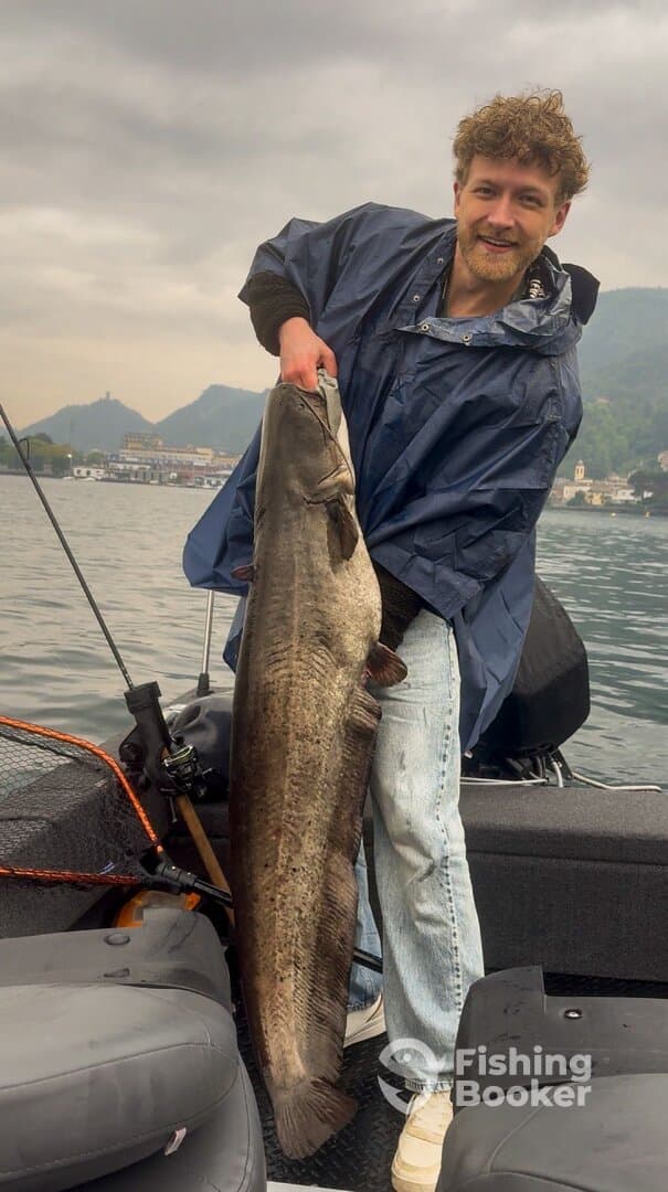 Angler proudly displaying a large catfish while fishing on a boat in a scenic lake environment.
