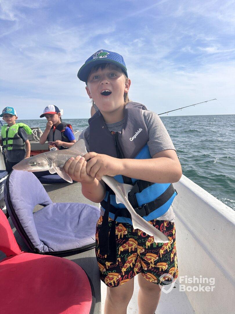 Excited young angler holding a small shark while fishing with friends on a boat, showcasing a fun day on the water.