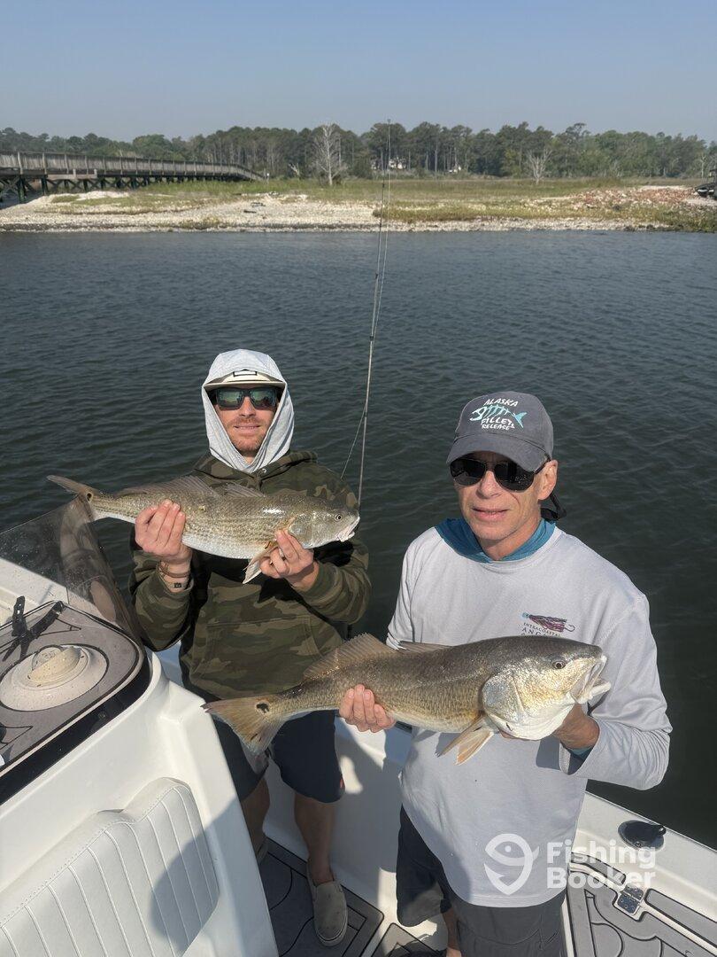 Two anglers proudly displaying their catches of Redfish while on a fishing trip, showcasing a beautiful day on the water.