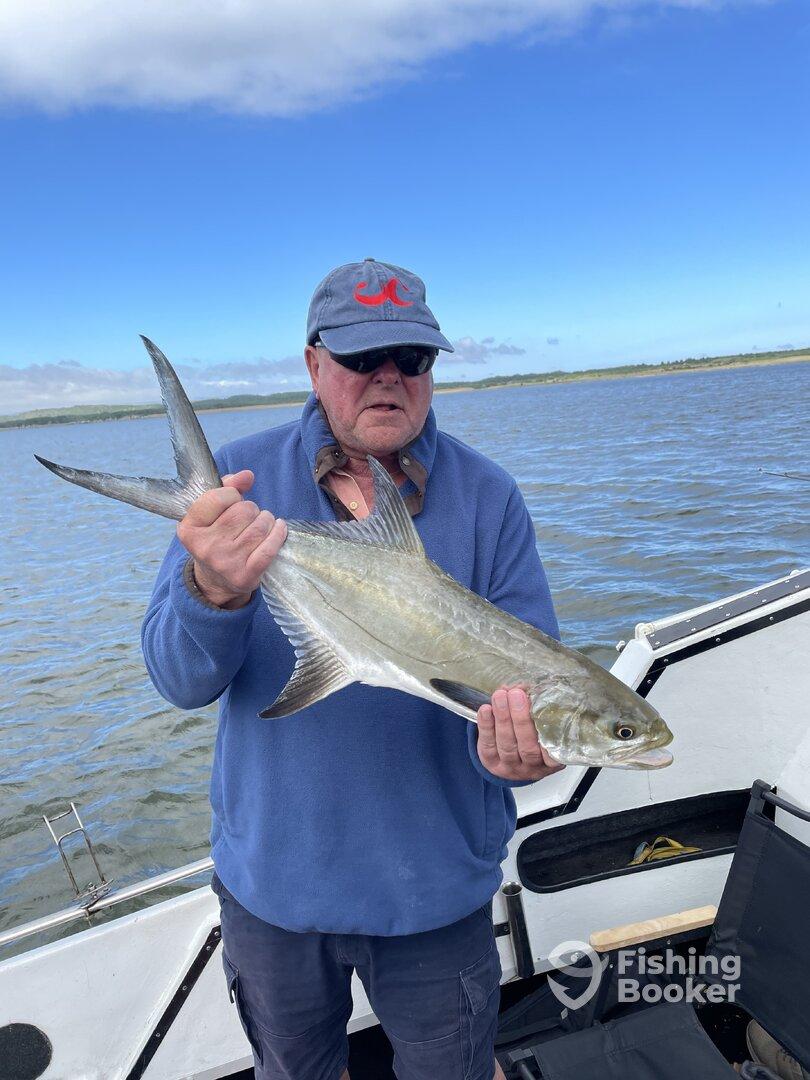 An angler proudly displaying a Silverfish while fishing on a boat in a scenic waterway.