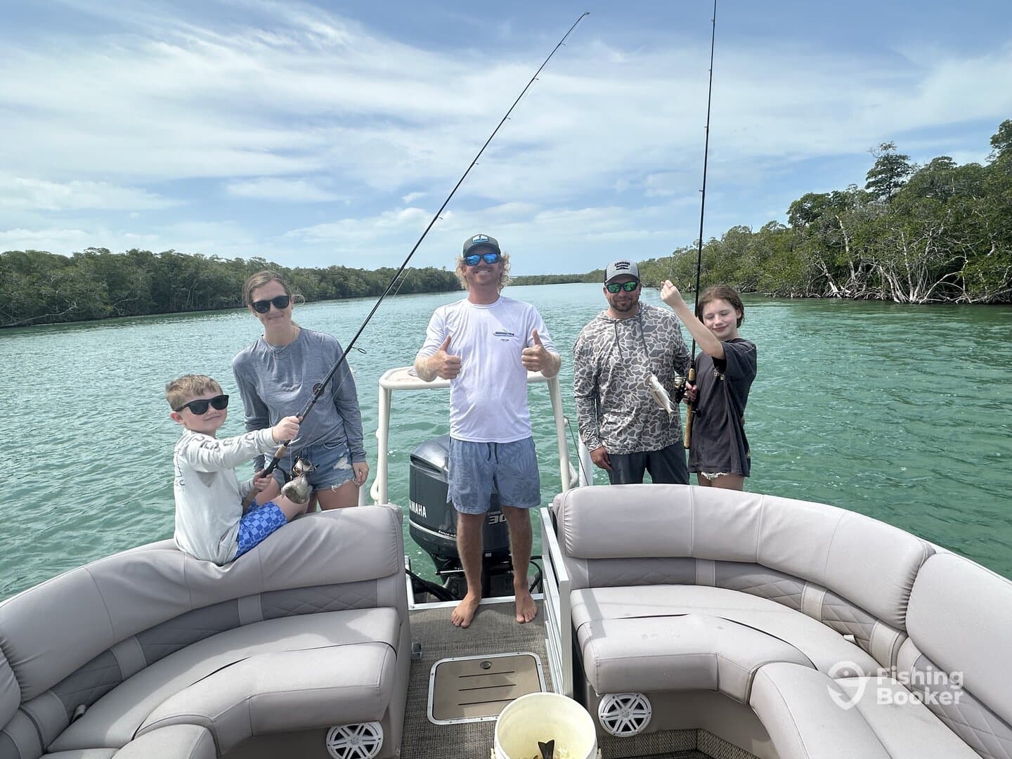 A family enjoying a fishing trip on a boat, with kids actively reeling in their catches in a scenic mangrove setting.