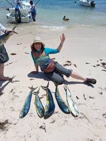 A happy angler poses with a catch of Mahi Mahi on the beach after a successful fishing trip.