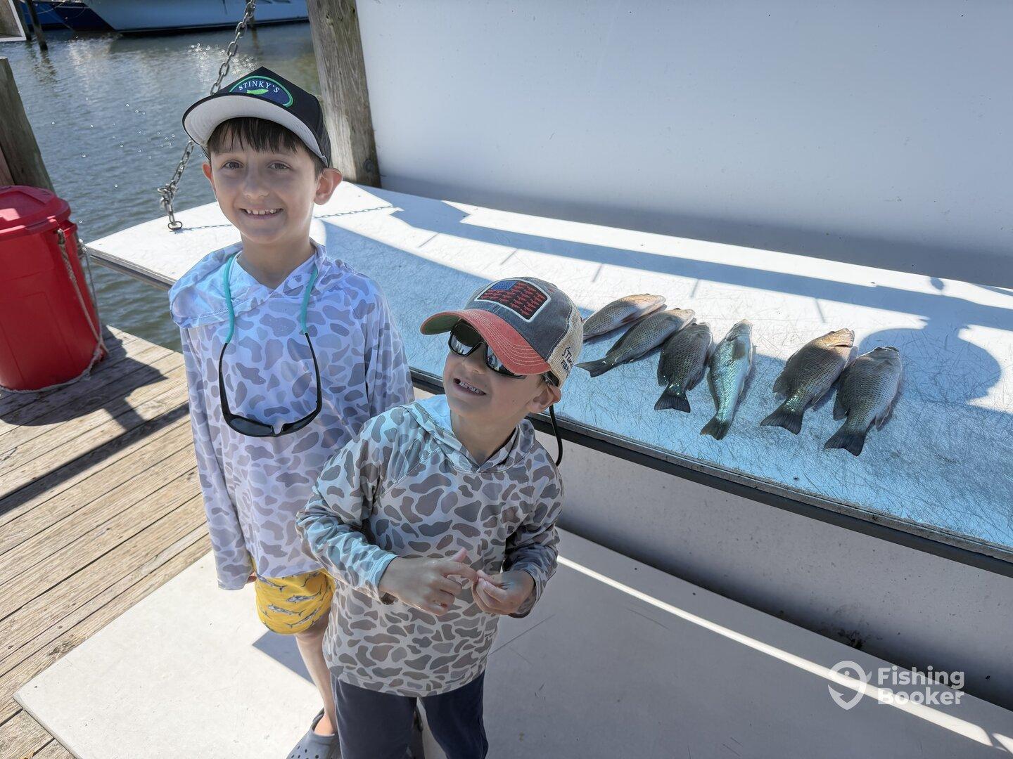 Two young anglers proudly posing next to their catch of several fish displayed on a cleaning table at the dock.