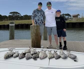 A family proudly displays their catch of several fish on a boat after a successful fishing trip.