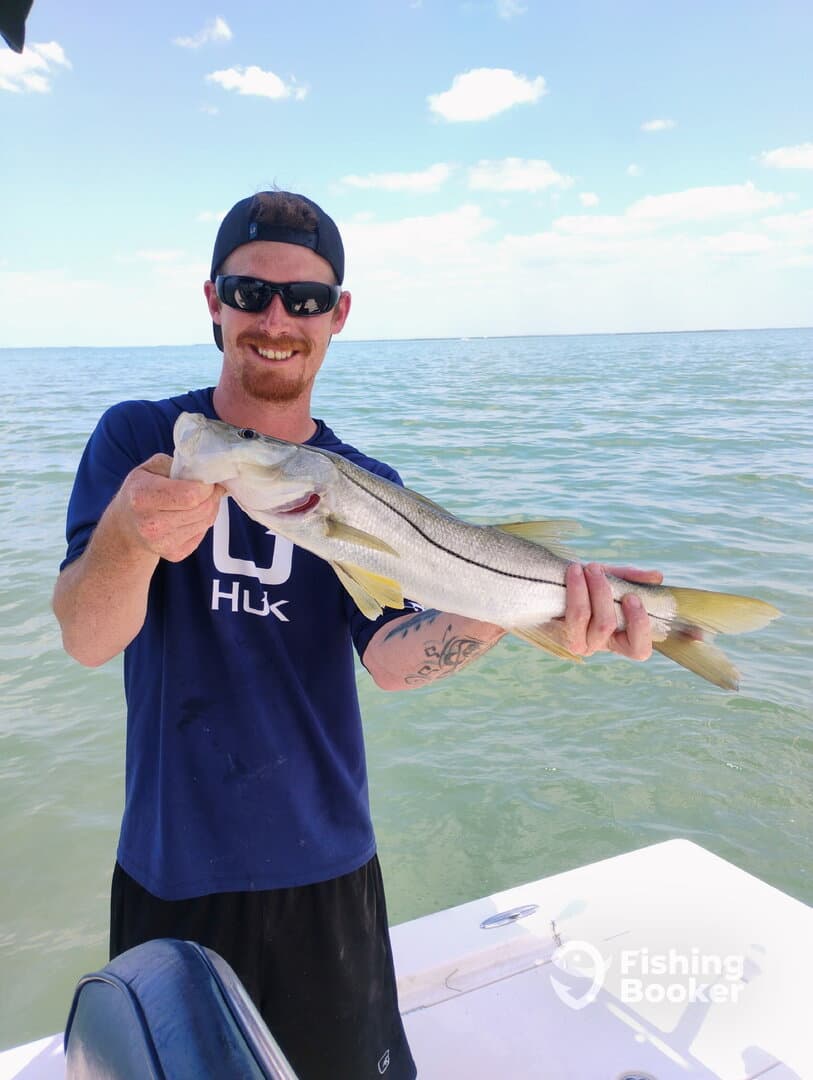 Angler proudly displaying a Snook while fishing on a sunny day in coastal waters.