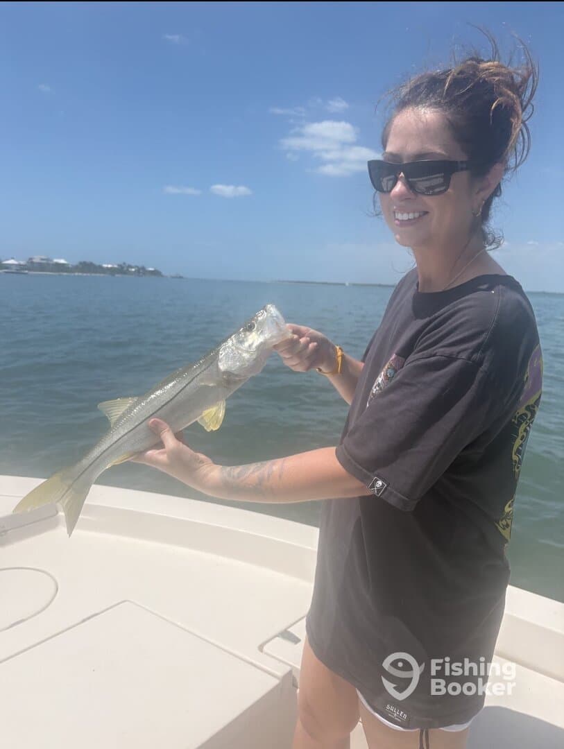 Angler proudly holding a Snook while fishing on a boat in sunny waters.