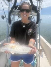 Angler proudly displaying a freshly caught Snook while aboard a fishing boat in calm waters.