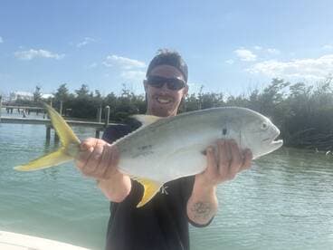 Angler proudly displaying a large Yellow Jack caught during a fishing trip in calm waters.