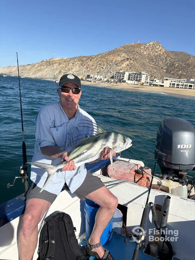 Angler proudly displaying a large fish while fishing from a boat near a scenic coastal backdrop.