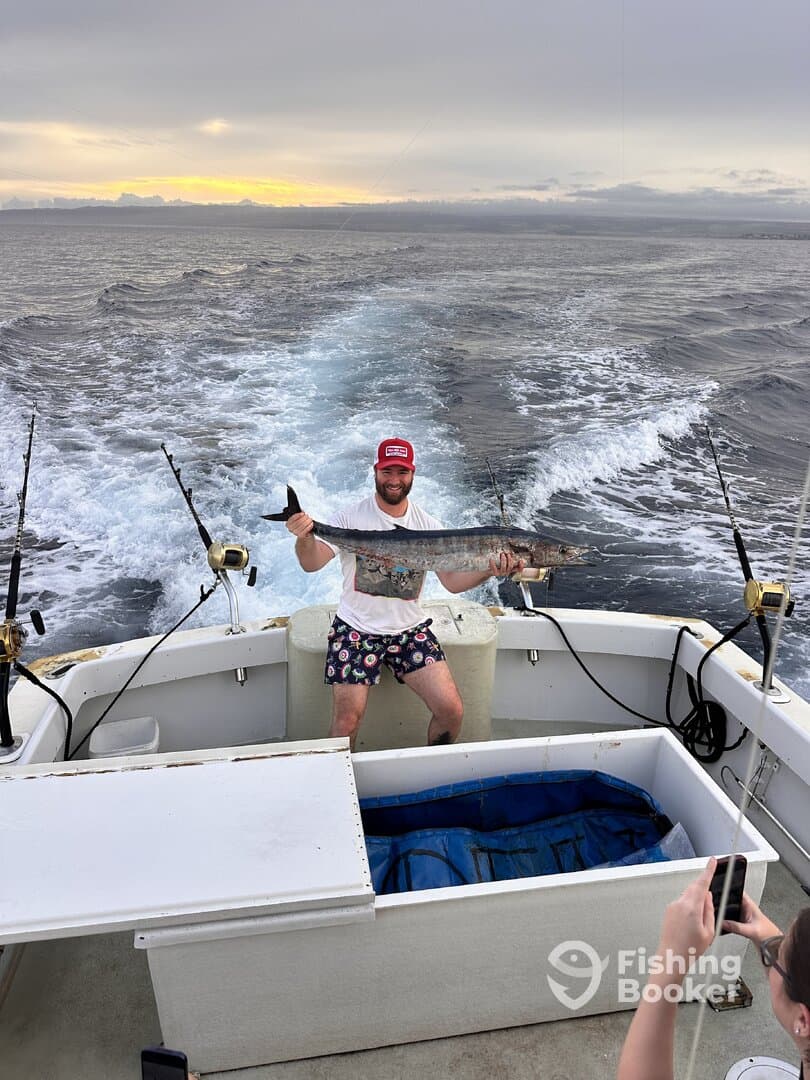 Angler proudly displaying a large fish aboard a fishing boat during a sunset trip, showcasing the excitement of a successful catch.