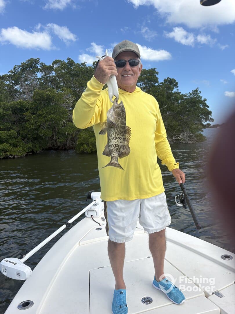 An angler proudly displaying a large grouper while fishing from a boat in a scenic coastal environment.