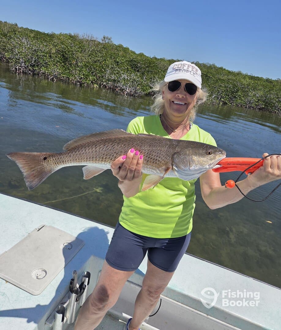 A proud angler displaying a large Redfish while fishing in a scenic coastal environment.