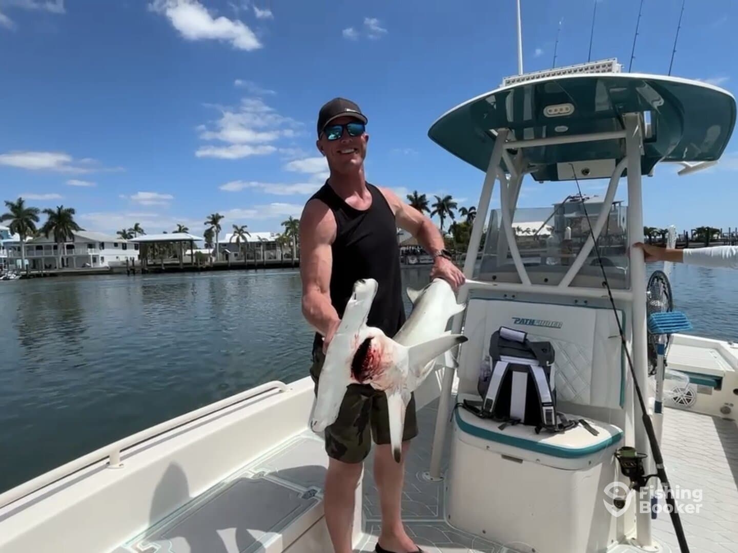 Angler proudly displaying a large shark on a boat in a scenic coastal setting.