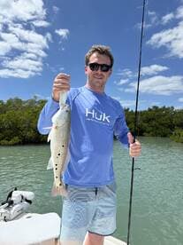 Angler proudly displaying a Speckled Trout while fishing in a scenic coastal environment.