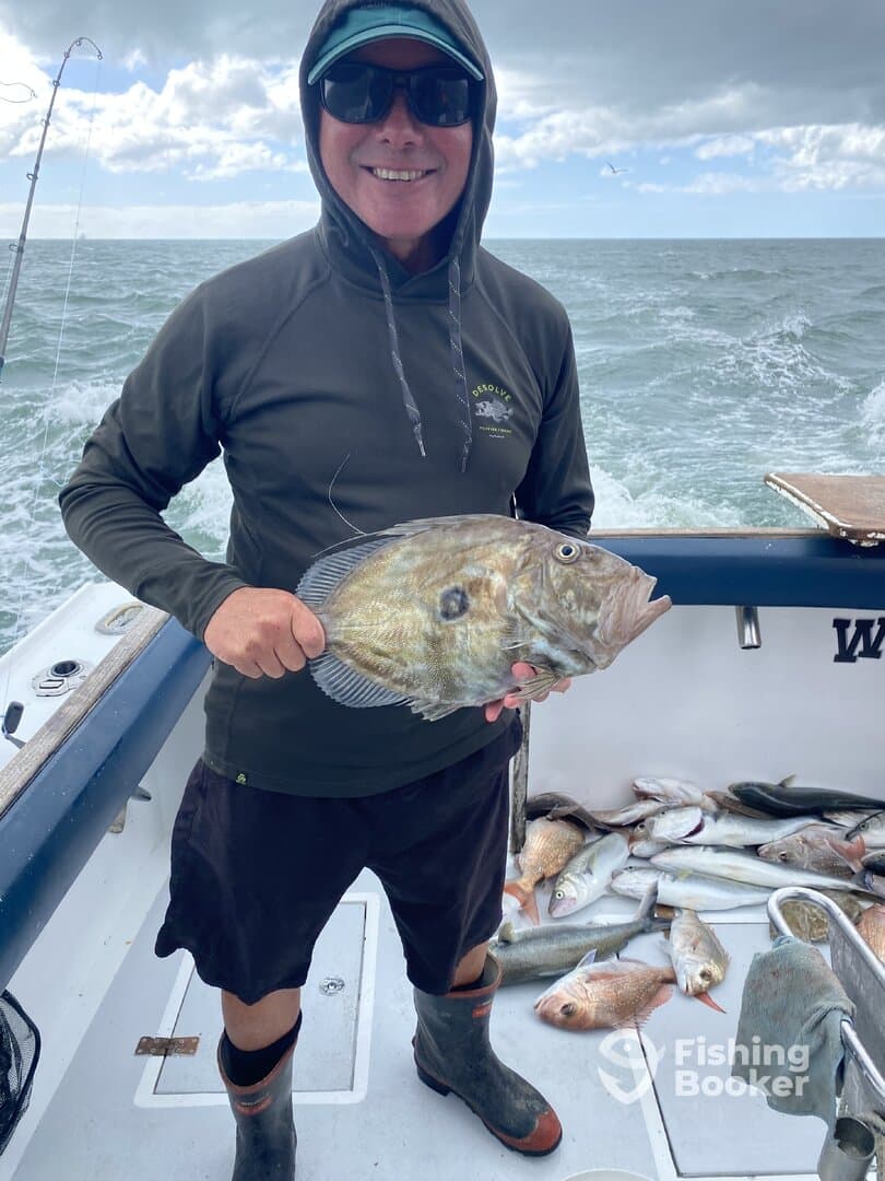 A smiling angler proudly displaying a large fish on a boat, surrounded by a variety of other catches on the deck.