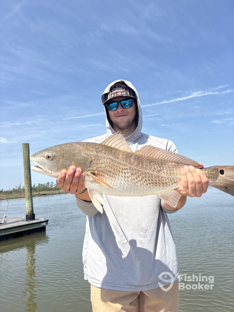 Angler proudly displaying a large Redfish while standing on a dock, showcasing a successful day of fishing.