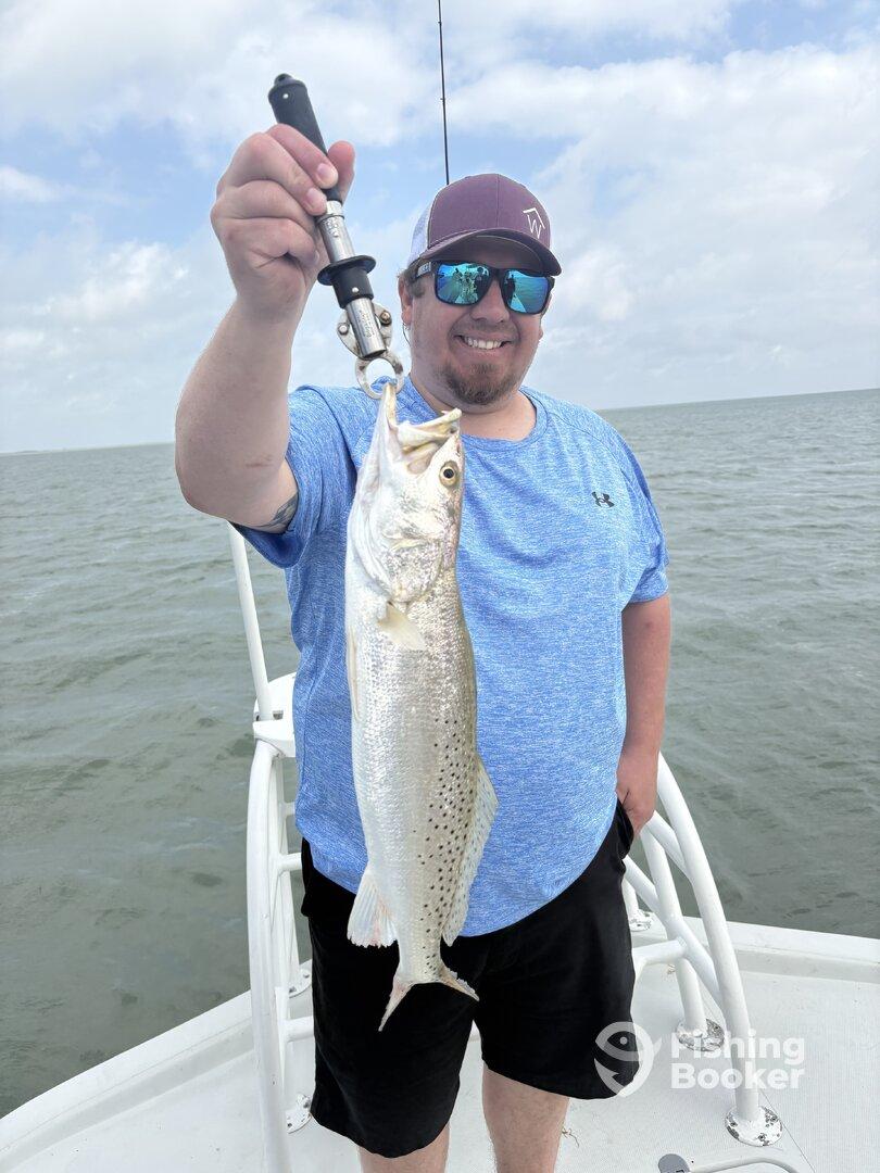 Angler proudly displaying a large Speckled Trout while fishing on a boat in open waters.