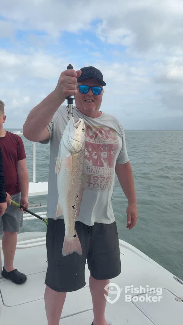A proud angler holding a large Redfish while fishing with family on a charter boat.